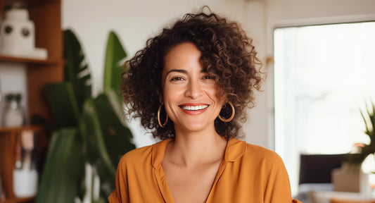 Curly haired woman in orange blouse smiling.